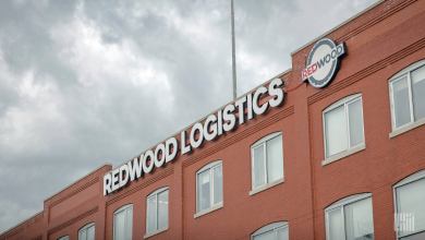 Redwood Logistics building exterior with large white “REDWOOD LOGISTICS” signage and circular logo on red brick facade