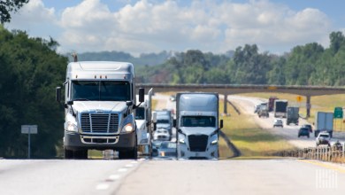 White semi-trucks driving on a busy multi-lane interstate highway under a sunny blue sky, representing the tightening truckload capacity driving higher rates in 2026