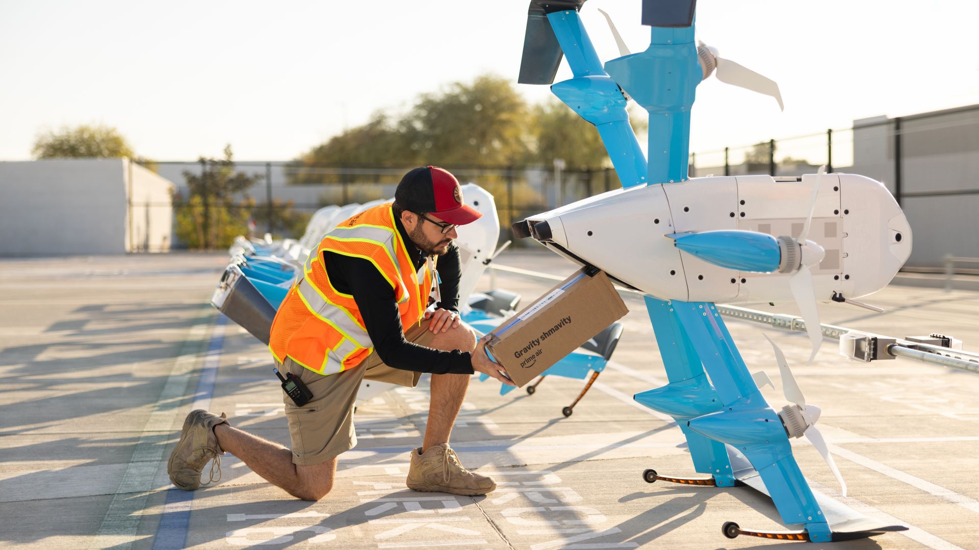 An Amazon worker loads a package into a light blue Prime Air delivery drone.