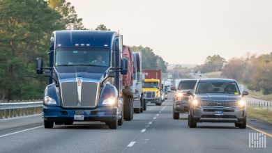 Blue semi-truck driving on a busy multi-lane highway with other trucks and vehicles at golden hour