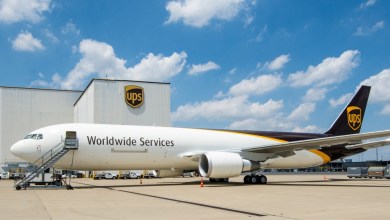Side view of a brown-tail UPS freighter next to a UPS terminal at an airport on a sunny day.