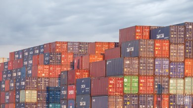 Stacks of colorful shipping containers from carriers like CMA CGM and APL at a port terminal, representing global freight and supply chain logistics.