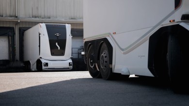 White Einride electric heavy-duty truck with distinctive black front panel parked next to a larger white semi-trailer at an industrial warehouse