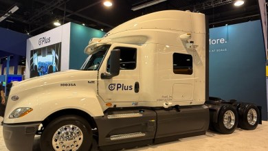 White PlusAI autonomous semi-truck with roof-mounted sensors and lidar on display at an industry expo, featuring prominent Plus branding on the cab of an International LT model