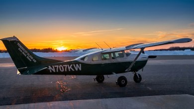 A small single-engine plane seen from the side with sun rising in background.