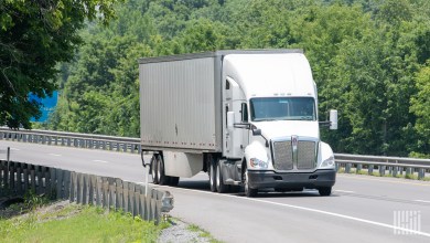 a white tractor pulling a trailer on a rural stretch of highway