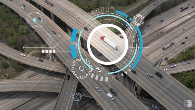 Aerial view of a busy highway interchange featuring a semi-truck highlighted with a white circular AI graphic and blue tech overlays of gears and data points.