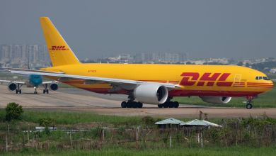 A bright-yellow DHL 777 cargo jet prepares for takeoff, turns onto runway as seen from right side.