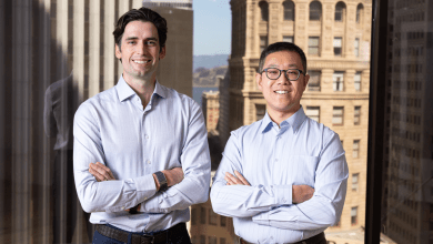 Loop co-founders Matt McKinney and Shaosu Liu stand with arms crossed and smiling in front of a large window overlooking the San Francisco skyline.
