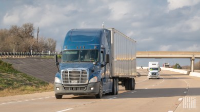 a blue tractor pulling a silver trailer on a highway