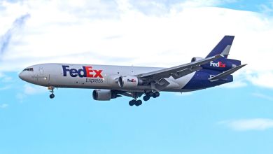 A purple-tailed MD-11 FedEx cargo jet approaches an airport with its wheels lowered.