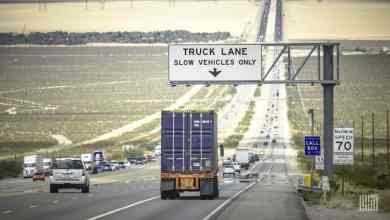 Heavy-duty semi-truck in the designated truck lane on a California highway under an overhead sign reading "TRUCK LANE SLOW VEHICLES ONLY"