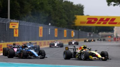 Formula 1 race cars go around a corner during a race with yellow-red DHL banners in the background.