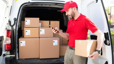 A man in a red shirt and red cap checks a stack of packages in the back of his van.