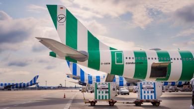 Back-half of striped Condor jets with small cargo containers parked by their side on the tarmac.