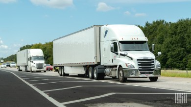 A pair of white sleeper cabs pulling trailers on a highway