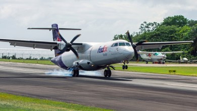 A purple-tailed FedEx twin-engine turboprop aircraft touches down on a runway with its rear wheels.