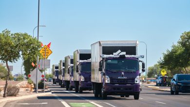 Convoy of purple Gatik autonomous Isuzu trucks driving on a sunny highway with sensor equipment on the lead vehicle