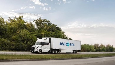 AVI-SPL Volvo VNL Autonomous truck used in new commercial freight operations, shown parked on a road next to trees, featuring company branding and autonomous driving sensors on the cab.