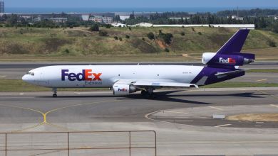 A side view of a purple-tailed FedEx MD-11 cargo jet, which sports three engines.