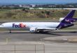 A side view of a purple-tailed FedEx MD-11 cargo jet, which sports three engines.