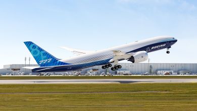 A large 777 jet in Boeing livery takes off from an airfield.