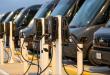 A row of electric vehicle chargers in front of a group of electric delivery vans