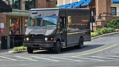 A brown UPS delivery van stops at a store at a strip mall.