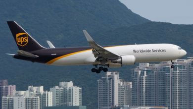 A brown-tailed UPS cargo jet approaches the airport with the Hong Kong skyline in the background.