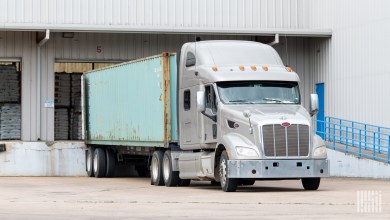 a silver tractor with an ocean container at a warehouse