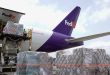 A view of the back third of a purple-tailed FedEx jet with pallets being lifted into through the side cargo door.