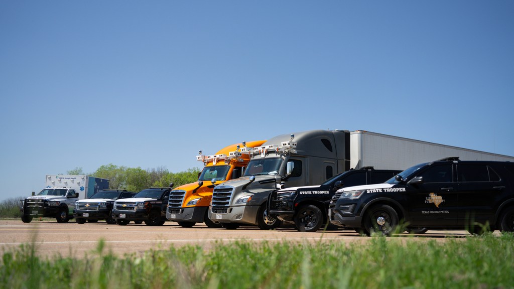 Bot Auto autonomous trucks lined up with Texas Highway Patrol SUVs and a first-responder ambulance