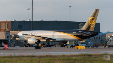 A brown-tailed UPS cargo jet is parked in front of a UPS terminal, as seen from the side rear.