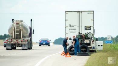 Technicians perform roadside tire service on a commercial truck parked on a highway shoulder