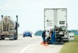 Technicians perform roadside tire service on a commercial truck parked on a highway shoulder