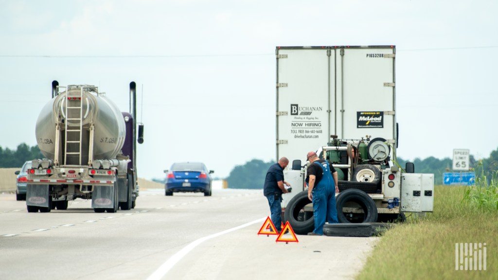 Technicians perform roadside tire service on a commercial truck parked on a highway shoulder