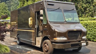 A brown UPS van stops on a neighborhood street to drop a package at a residence.