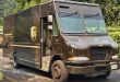 A brown UPS van stops on a neighborhood street to drop a package at a residence.