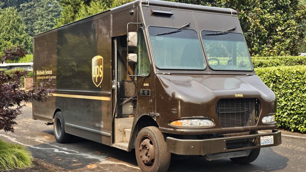 A brown UPS van stops on a neighborhood street to drop a package at a residence.