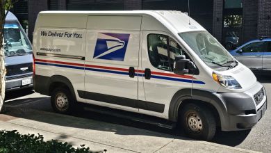 Side view of a modern U.S. Postal Service delivery van parked on a city street.