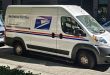 Side view of a modern U.S. Postal Service delivery van parked on a city street.