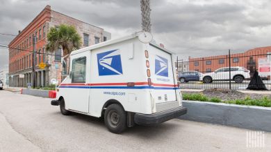 Angled view of a U.S. Postal Service delivery van driving in a small city.