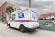 Angled view of a U.S. Postal Service delivery van driving in a small city.