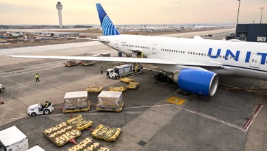 Overhead view of a United Airlines jet on the ramp at Dulles Airport on a sunny day as a tug moves cargo containers on the ground.