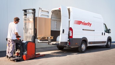 A man with a small forklift loads a box into the pack of a Priority van.