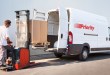 A man with a small forklift loads a box into the pack of a Priority van.