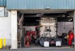 Technicians service a heavy-duty truck in a shop bay, where fleet repair costs concentrate.