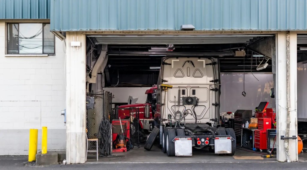 Technicians service a heavy-duty truck in a shop bay, where fleet repair costs concentrate.