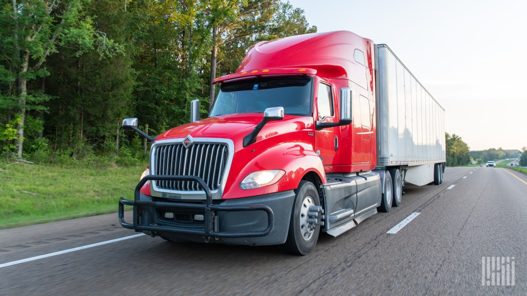 a red sleeper cab pulling a white trailer on a highway