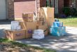 Amazon, FedEx, USPS and Walmart parcel boxes stacked in a residential driveway.